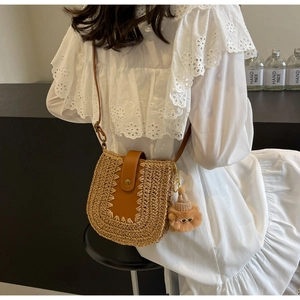 Sac à bandoulière en paille avec lanière en cuir porté par un mannequin en robe blanche