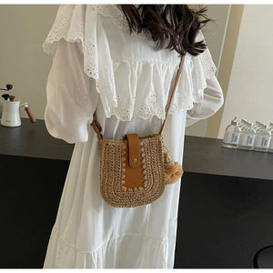 Sacoche en paille avec rabat en cuir marron et pompon porté sur robe en dentelle