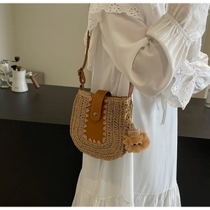 Detail of woven straw bucket bag featuring brown leather flap and stylish plush charm