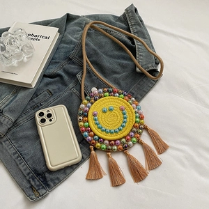 Handwoven yellow round crossbody bag featuring a beaded smiley face and brown tassels