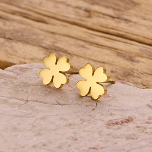 Detail shot of golden four-leaf clover stud earrings on natural light pink stone