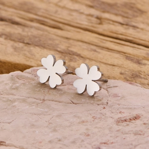 Minimalist four-leaf clover stud earrings in polished silver metal on natural rock