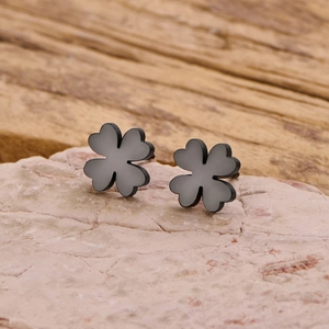 Close-up of minimalist black four-leaf clover stud earrings on a natural stone surface