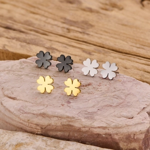 Three pairs of clover stainless steel studs in black, silver, and gold on rock