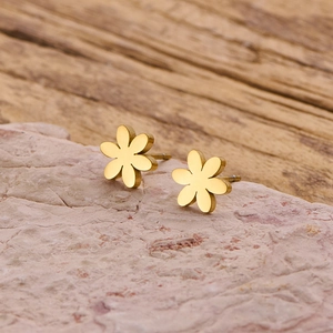 Détail macro de boucles d'oreilles fleur dorées avec fini mat sur pierre brute rose