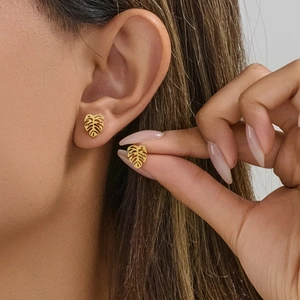 Golden monstera leaf stud earrings in stainless steel on ear and held by fingers