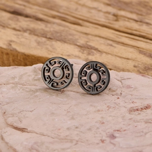 Macro shot of matte black hollow geometric round stud earrings on a textured stone