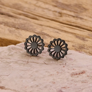 Gros plan des boucles d'oreilles fleurs noir mat de 10mm sur une surface en pierre rose