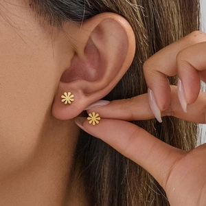 Minimalist stainless steel daisy stud earrings in gold worn on earlobe for size reference