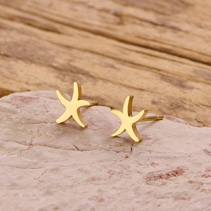 Macro shot of polished gold starfish stud earrings resting on a natural stone surface