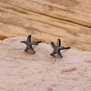 Macro shot of minimalist starfish stud earrings in dark metal on a textured surface