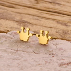 Detail view of gold crown stud earrings placed on a natural stone with a warm wood background