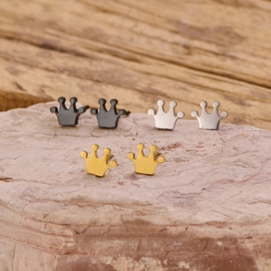 Three pairs of stainless steel crown earrings in gold, silver, and black on a stone base