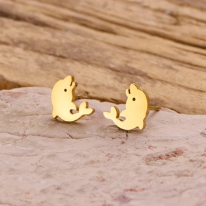 Macro shot of minimalist gold dolphin stud earrings on a natural pink stone surface