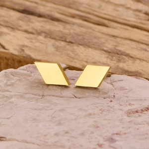 Macro shot of minimalist gold geometric quadrilateral stud earrings on natural stone