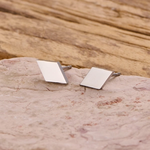 Minimalist silver rhombus stud earrings in stainless steel on a natural stone background