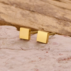 Close-up of minimalist gold square stud earrings on a textured stone display