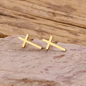 Detail of minimalist gold cross stud earrings resting on a natural pink stone surface