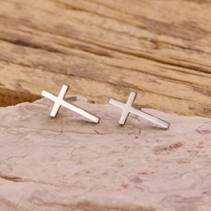 Polished stainless steel cross stud earrings for men and women on a rustic stone background