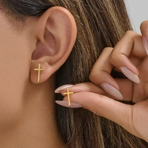 Minimalist gold cross stud earrings for men and women shown on a model's ear