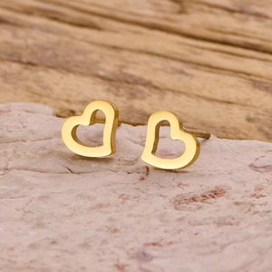 Gros plan de boucles d'oreilles cœur dorées ajourées sur pierre avec fond en bois chaleureux