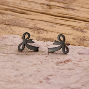 Detailed close-up of matte black stainless steel bow stud earrings on a stone surface