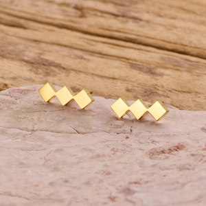 Detail of gold geometric rhombus stud earrings on stone and wood background