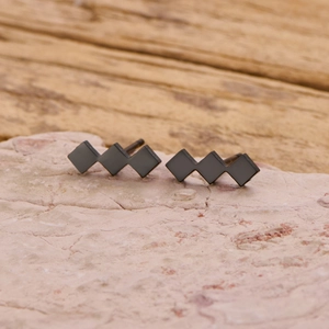 Close-up of geometric matte black earrings with three connected diamond shapes