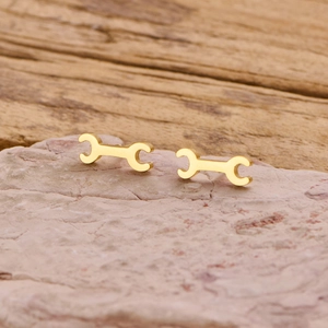 Detailed close-up of gold-plated gothic wrench stud earrings on a natural stone surface
