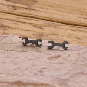 Detailed view of black wrench stud earrings in industrial punk style on a stone background