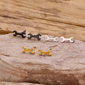 Gothic punk wrench stud earrings in black, gold, and silver on natural pink rock