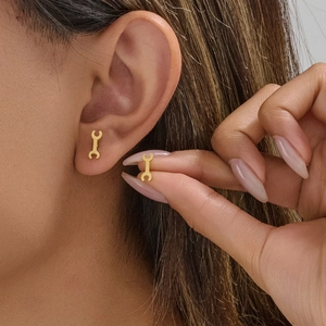 Minimalist punk style gold wrench stud earrings on ear for a modern fashion look