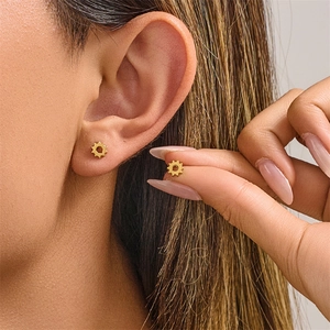 Detail view of retro gold gear-shaped stainless steel stud earring on earlobe