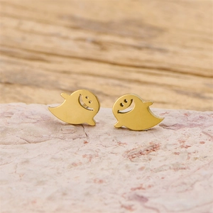 Close-up of gold ghost earrings with hollow smile design on a pink textured stone surface