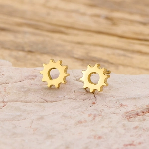 Detailed view of gold gear shaped stainless steel stud earrings on stone surface