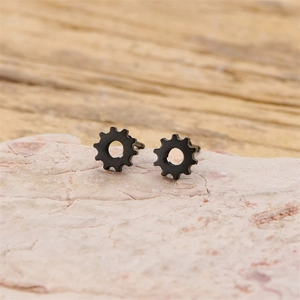 Detailed close-up of minimalist black gear stud earrings on a textured stone surface
