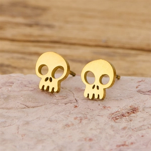 Macro shot of gold skull earrings with punk hollow design on pink stone background