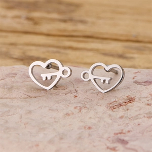Polished silver heart and key earrings displayed on a natural pink stone surface