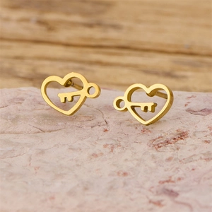 Macro shot of gold heart-shaped key stud earrings on pink textured stone base