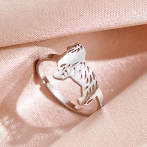 Eleganter silberner offener Ring mit hohler Hundesilhouette auf weichem rosa Seidenhintergrund