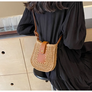 Modèle portant un sac besace en paille avec bordure en cuir marron et boucles