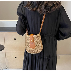 Détail d'un sac bandoulière en paille avec rabat en cuir brun et boucle dorée