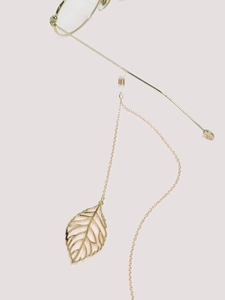 Detail view of gold metal eyewear chain with a delicate hollow leaf pendant on neutral background