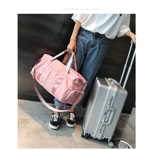 Pink fitness bag with shoe compartment and adjustable strap next to a silver suitcase