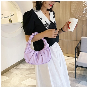 Close-up of a lilac ruched crescent shoulder bag in PU leather held in a cafe setting