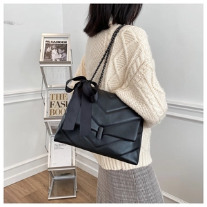 Close-up of black quilted chain bag featuring a decorative satin ribbon bow and V-stitch