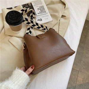 Detail of brown leather bucket bag with chevron strap on beige suit and coffee cup