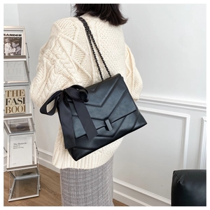 Detail of black quilted shoulder bag with large bow and metal chain strap on model