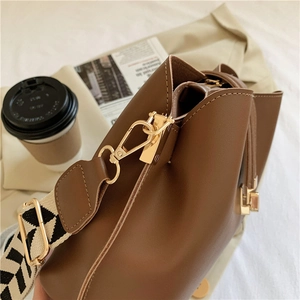 Close-up of brown leather bucket bag with gold metal hardware and geometric strap
