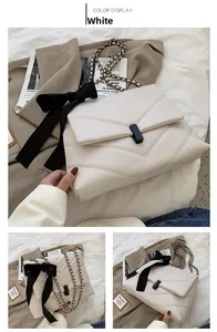 Detail of cream white quilted crossbody bag with a large black bow and metal chain strap